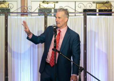 L.J Ganser behind the microphone in a blue suit, red shirt and red patterned tie as auctioneer for the 2019 Wild Bird Flocktail Party