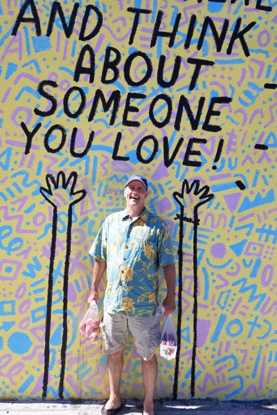 L.J. Ganser standing in front of a Keith Haring mural that reads "AND THINK ABOUT SOMEONE YOU LOVE!'